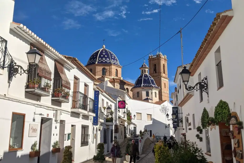 altea A view of a narrow street in Altea with white washed buildings and the blue dome of the church
