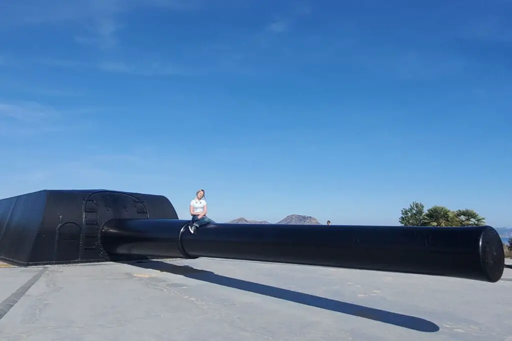 girl sat on a black naval gun at Cabo Tiñoso